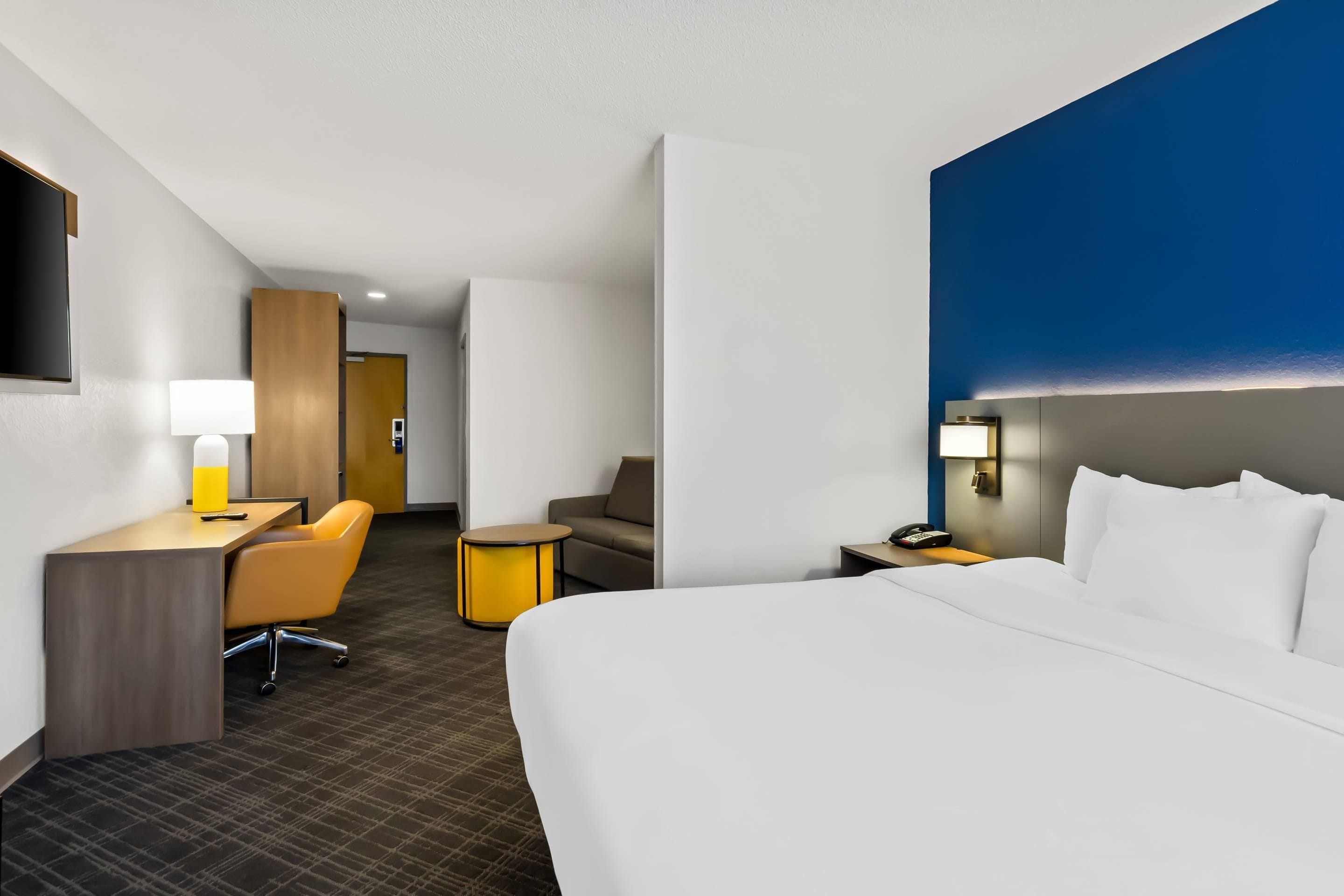 A hotel room with a bed, desk, chair, and a small table.