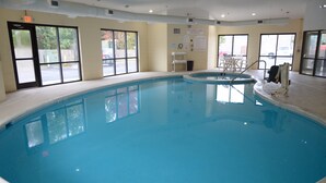 Una amplia piscina interior con paredes de vidrio transparente, una estación de socorristas y un área de descanso con sillas.