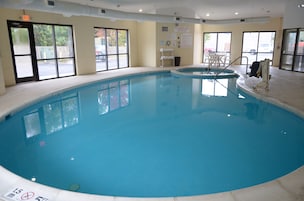 Uma grande piscina interior com paredes de vidro transparente, posto de salva-vidas e área de estar com cadeiras.