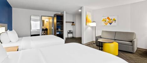 Une chambre d’hôtel avec deux lits, un canapé, une petite table et un pouf jaune.