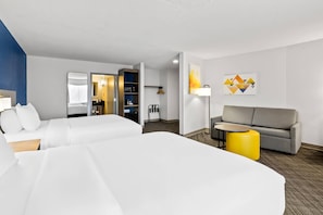 A hotel room with two beds, a sofa, a small table, and a yellow ottoman.