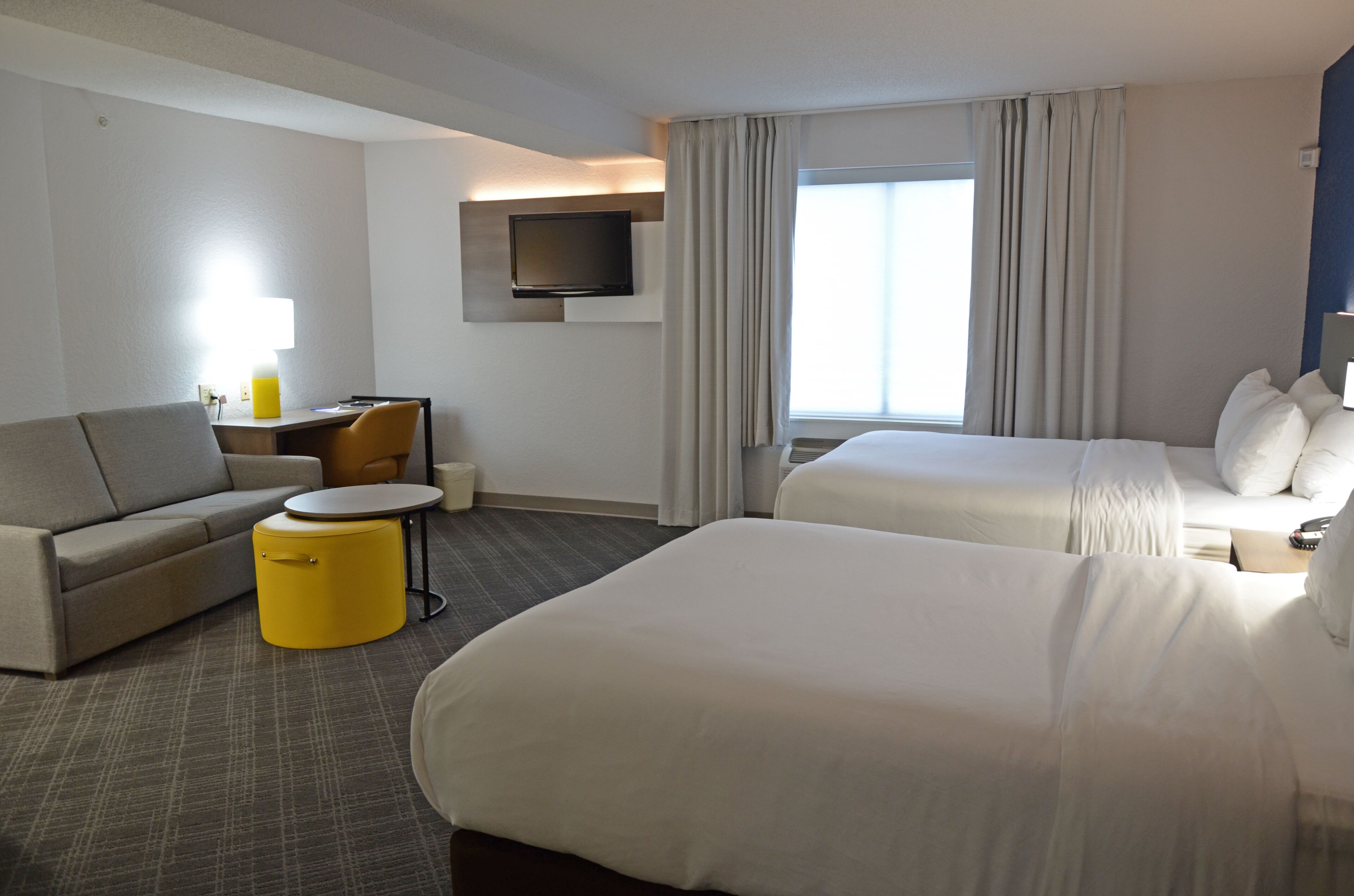 A hotel room with a sofa, a small round table, a bed, and a TV mounted on the wall.