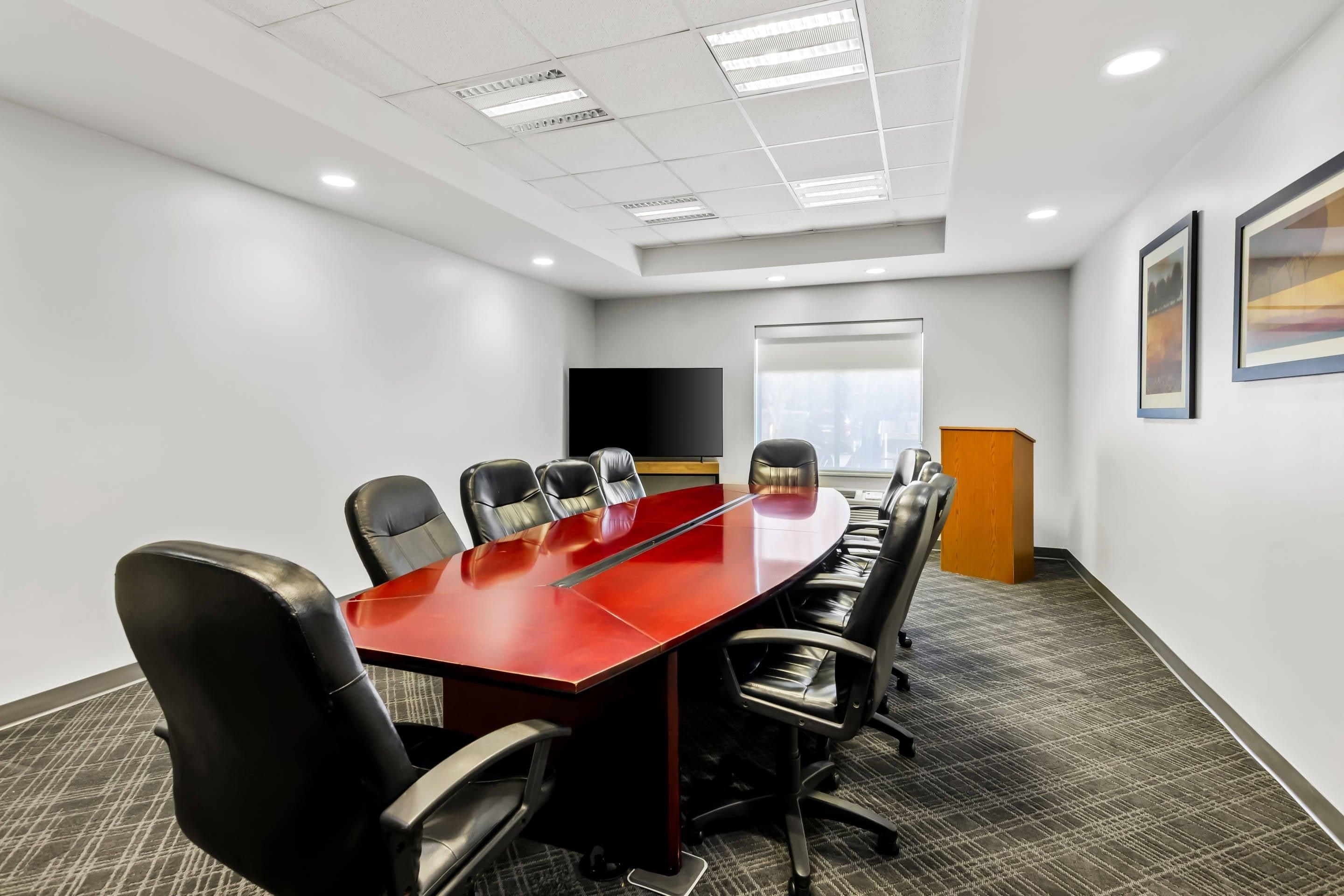 Une salle de conférence avec une longue table rouge, des chaises noires, un pupitre et une grande fenêtre.