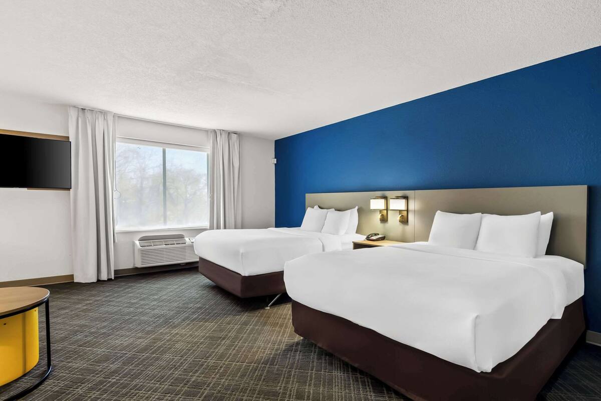 Hotelkamer met twee bedden, een flatscreen televisie aan de muur, een bureau met stoel en een raam met gordijnen.