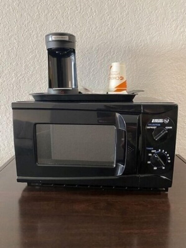 Een zwarte magnetronoven met een koffiezetapparaat en een fles water erop.