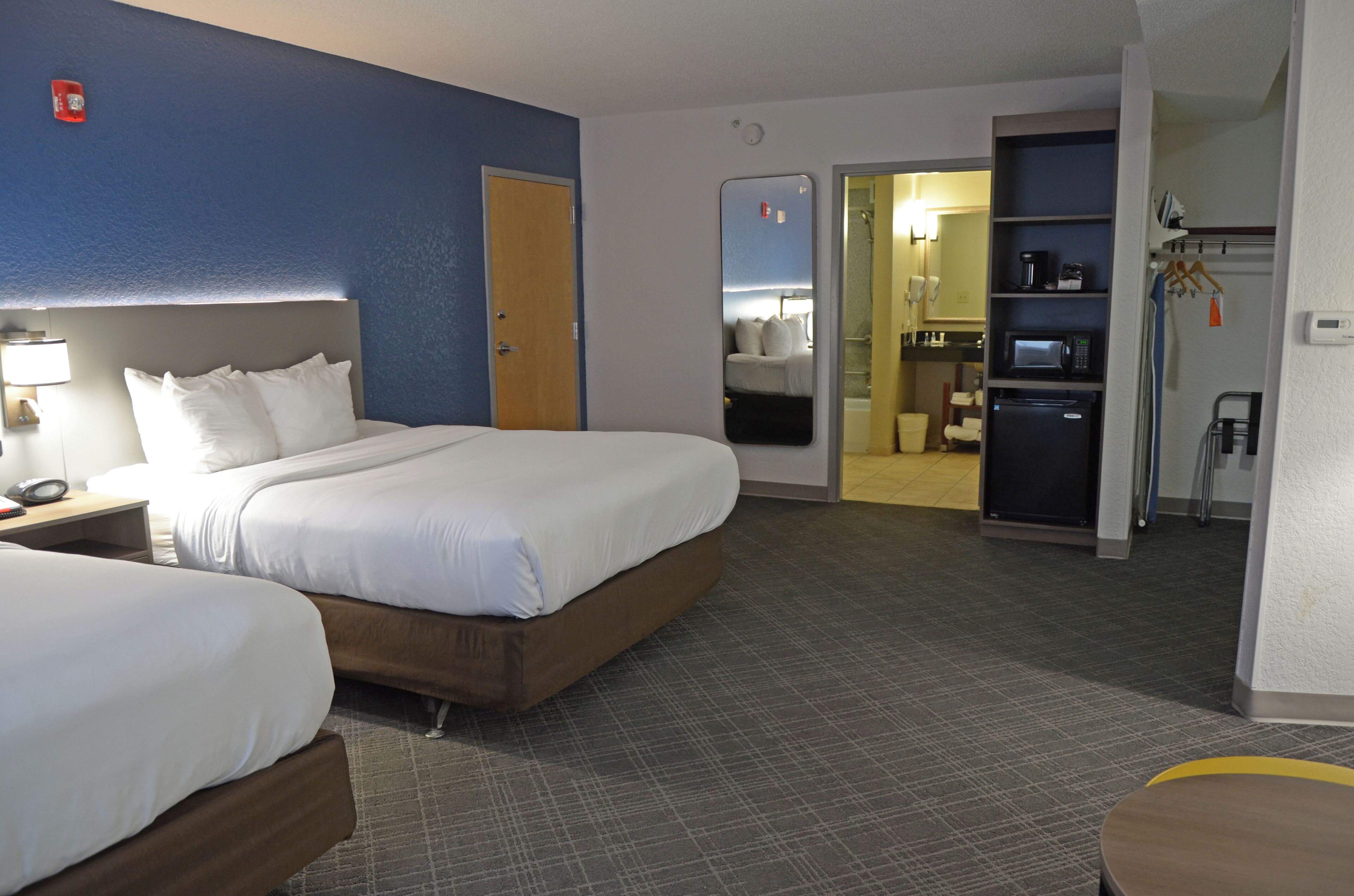 Quarto de hotel com duas camas, banheiro e cozinha compacta.