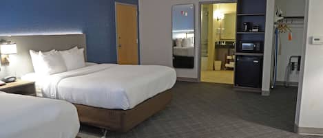 Quarto de hotel com duas camas, banheiro e cozinha compacta.