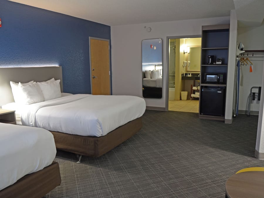 Quarto de hotel com duas camas, banheiro e cozinha compacta.