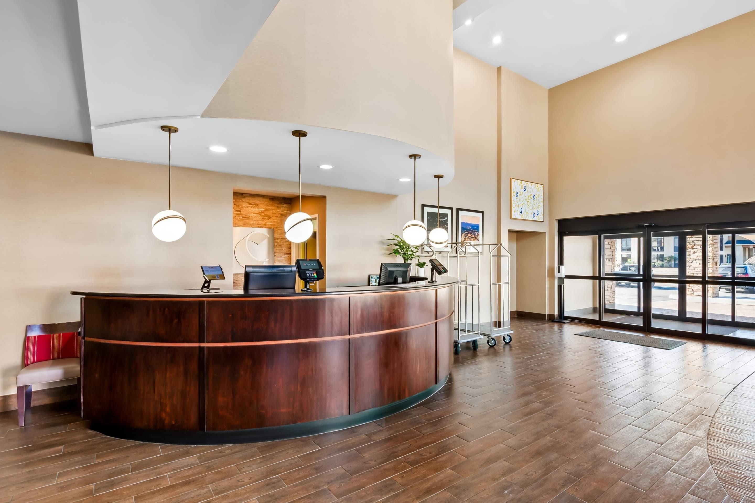 A reception area with a wooden reception desk, multiple light fixtures, a digital kiosk, and a view through large glass doors.