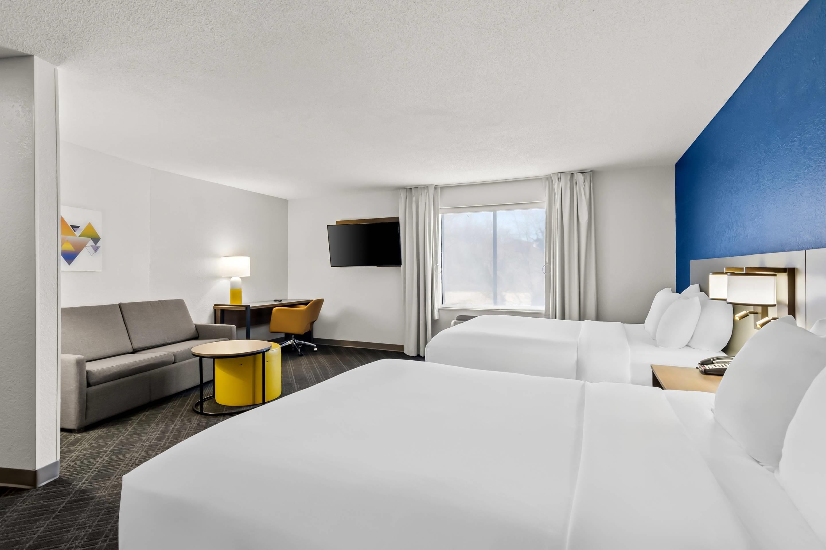 A hotel room with a bed, a sofa, a desk, a TV, and a window with curtains.