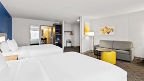 Ein Hotelzimmer mit zwei Betten, einem Schlafsofa, einem kleinen Tisch, einer Lampe und einem Bücherregal.