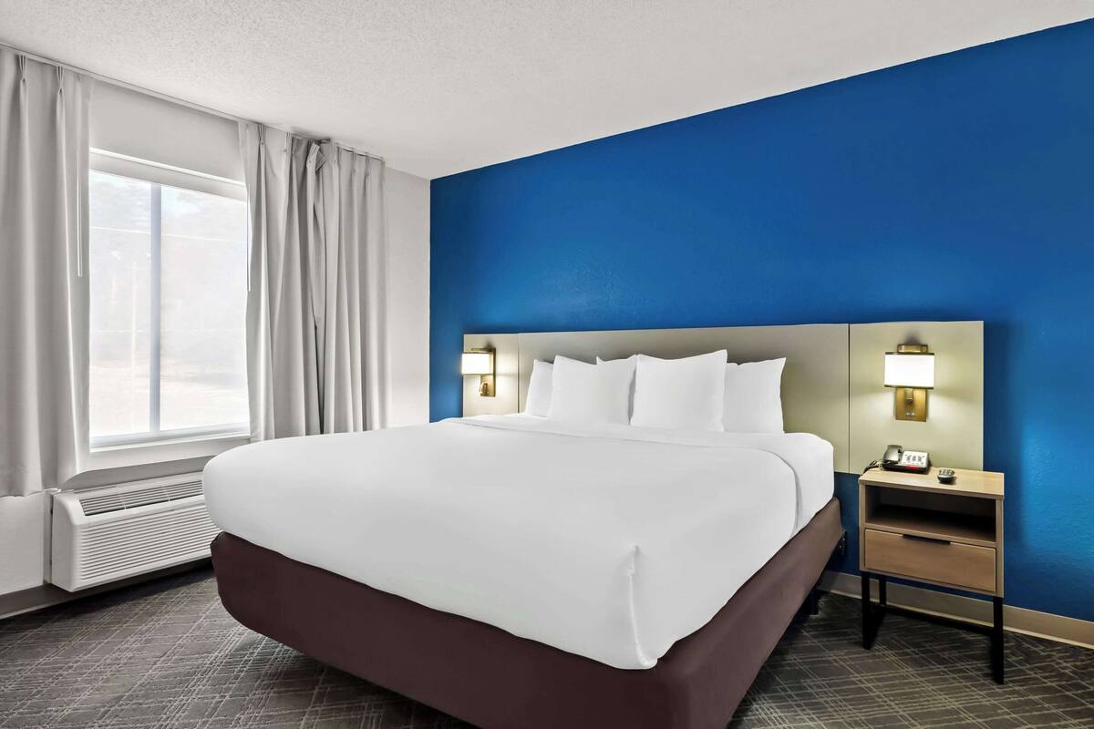 Hotelkamer met een groot bed, een nachtkastje met een lamp en uitzicht op het buitenland door het raam.
