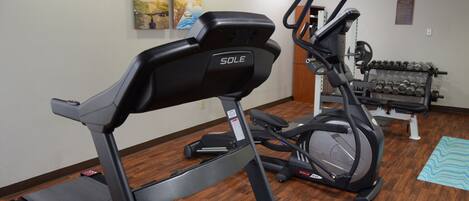 A home gym with a treadmill, elliptical, and dumbbells.