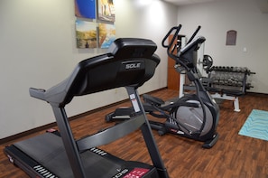 Een huisgym met een loopband, elliptische trainer en gewichten.