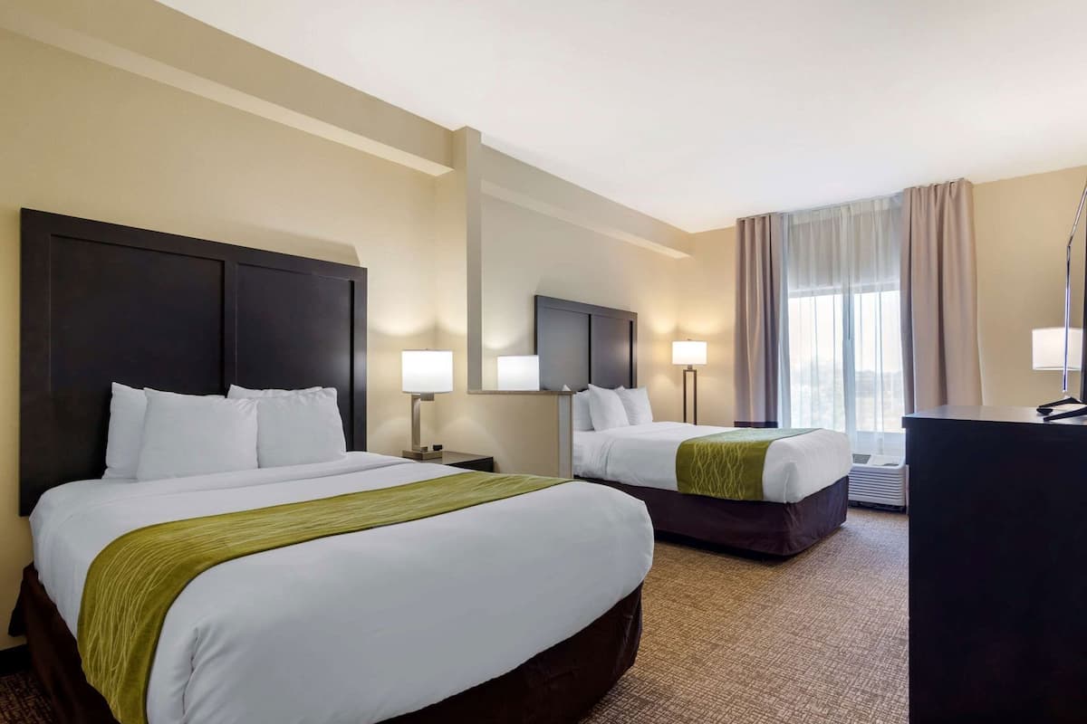 A hotel room with two beds, a desk, a chair, a TV, and a window with curtains.