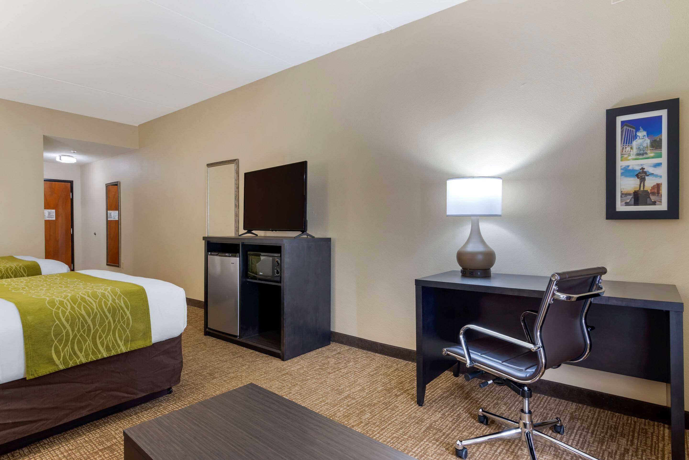 Een hotelkamer met twee bedden, een bureau met stoel, een televisie, een lamp en een ingelijst schilderij aan de muur.