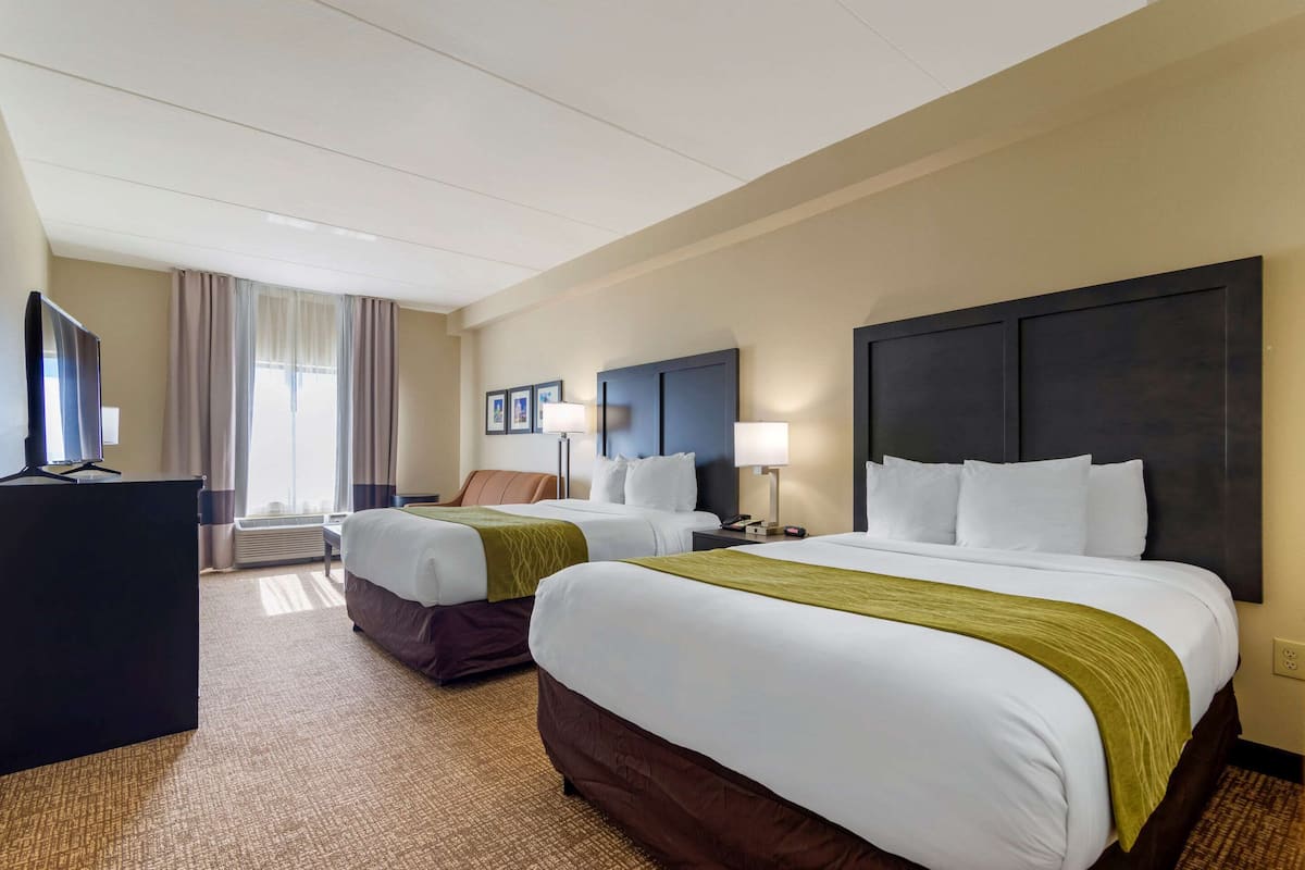 A hotel room with two beds, a desk, and a television.
