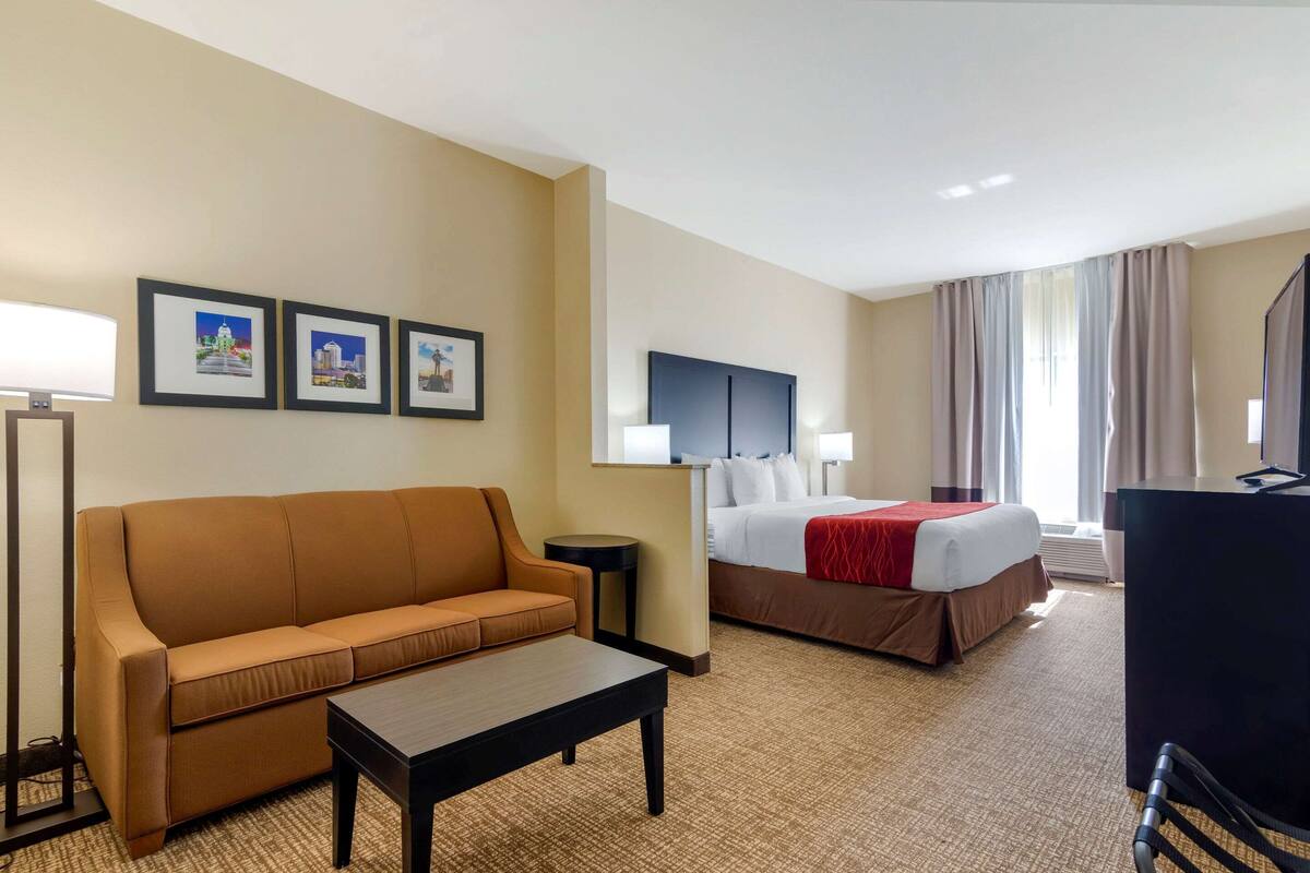 A hotel room with a sofa, a bed, a desk, and a TV. There are three framed pictures on the wall.