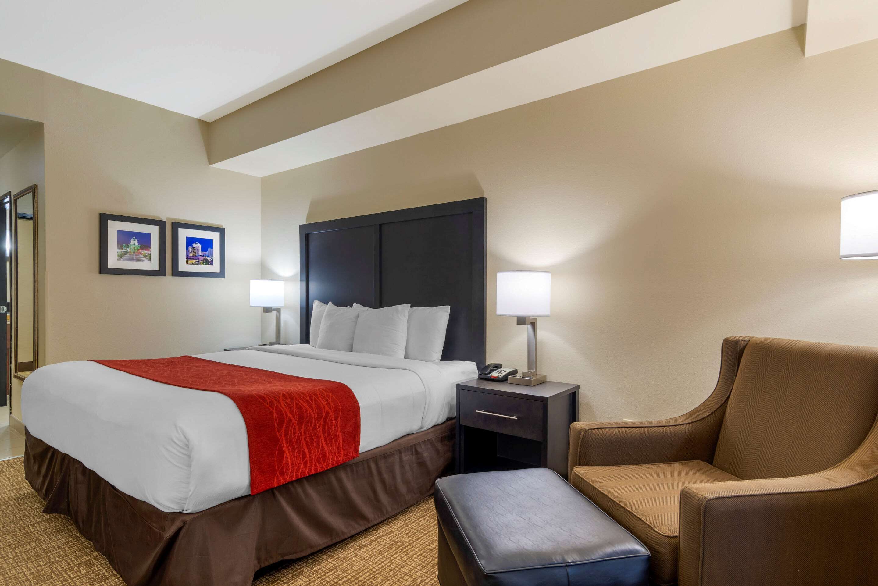 Habitación de hotel con una cama grande, una mesita de noche con lámpara, una silla y dos cuadros en la pared.