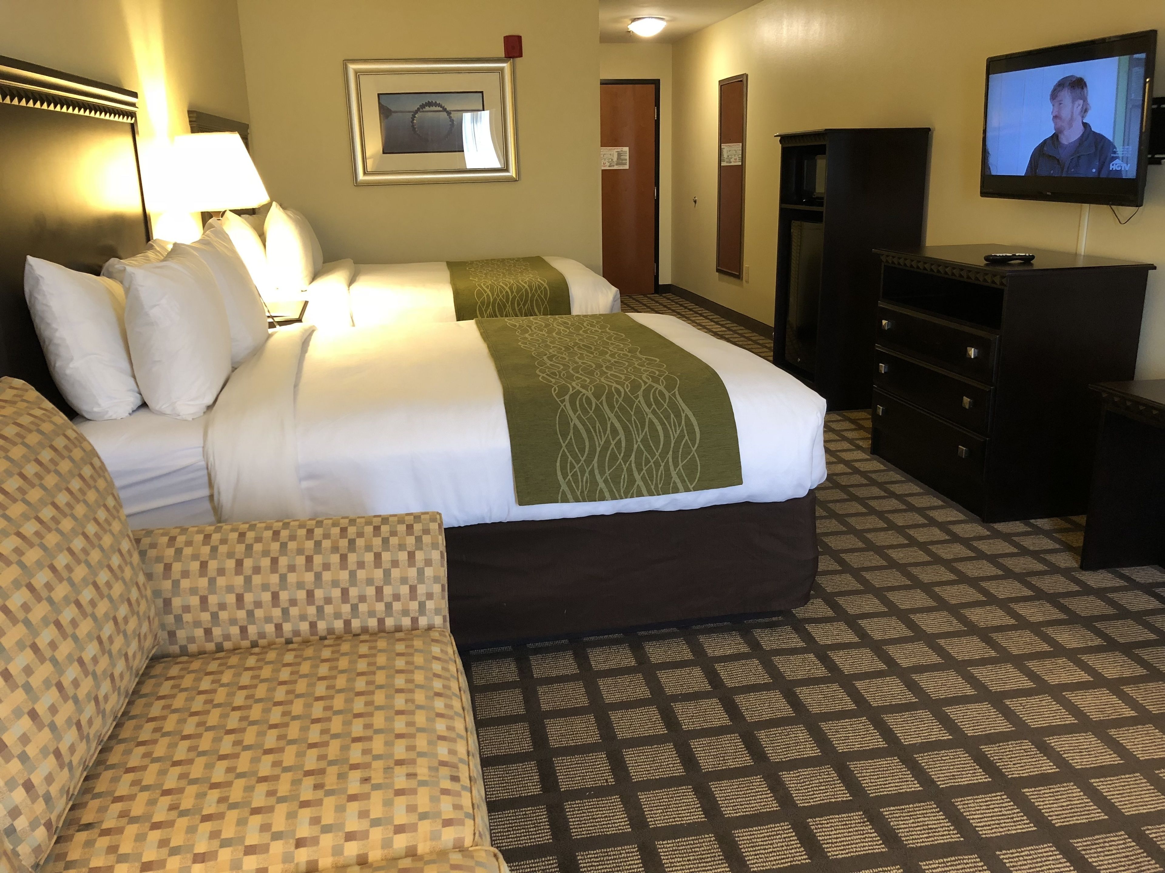 A hotel room with two beds, a sofa, a TV, and a dresser.