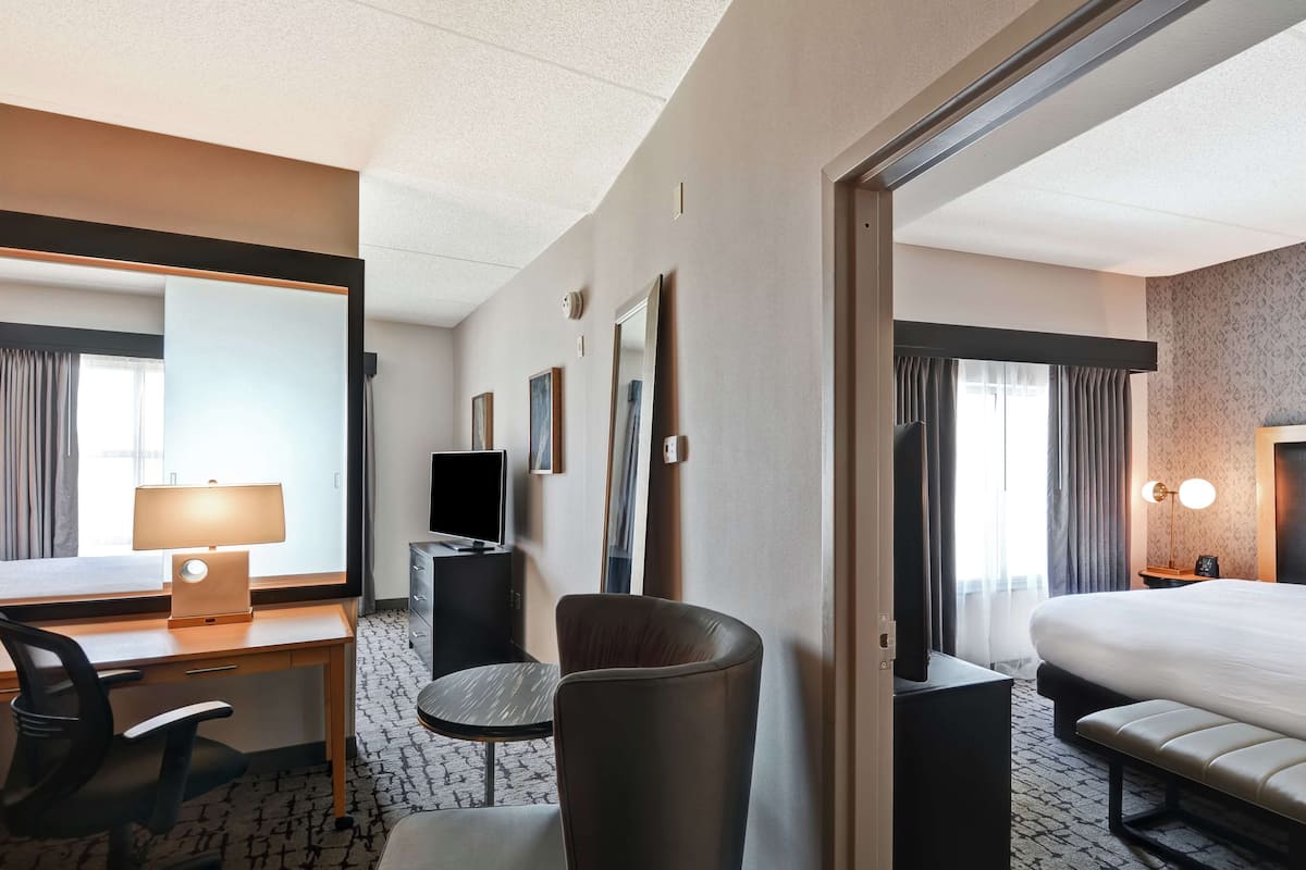 A hotel room with a bed, a desk with a lamp, a chair, a TV, and a large mirror.