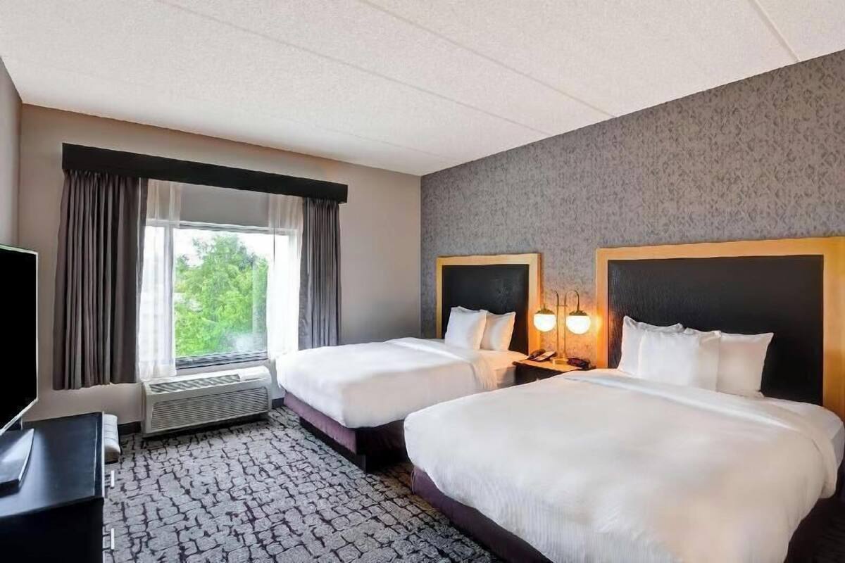 A hotel room with two beds, a television, a heater, and a window with curtains.