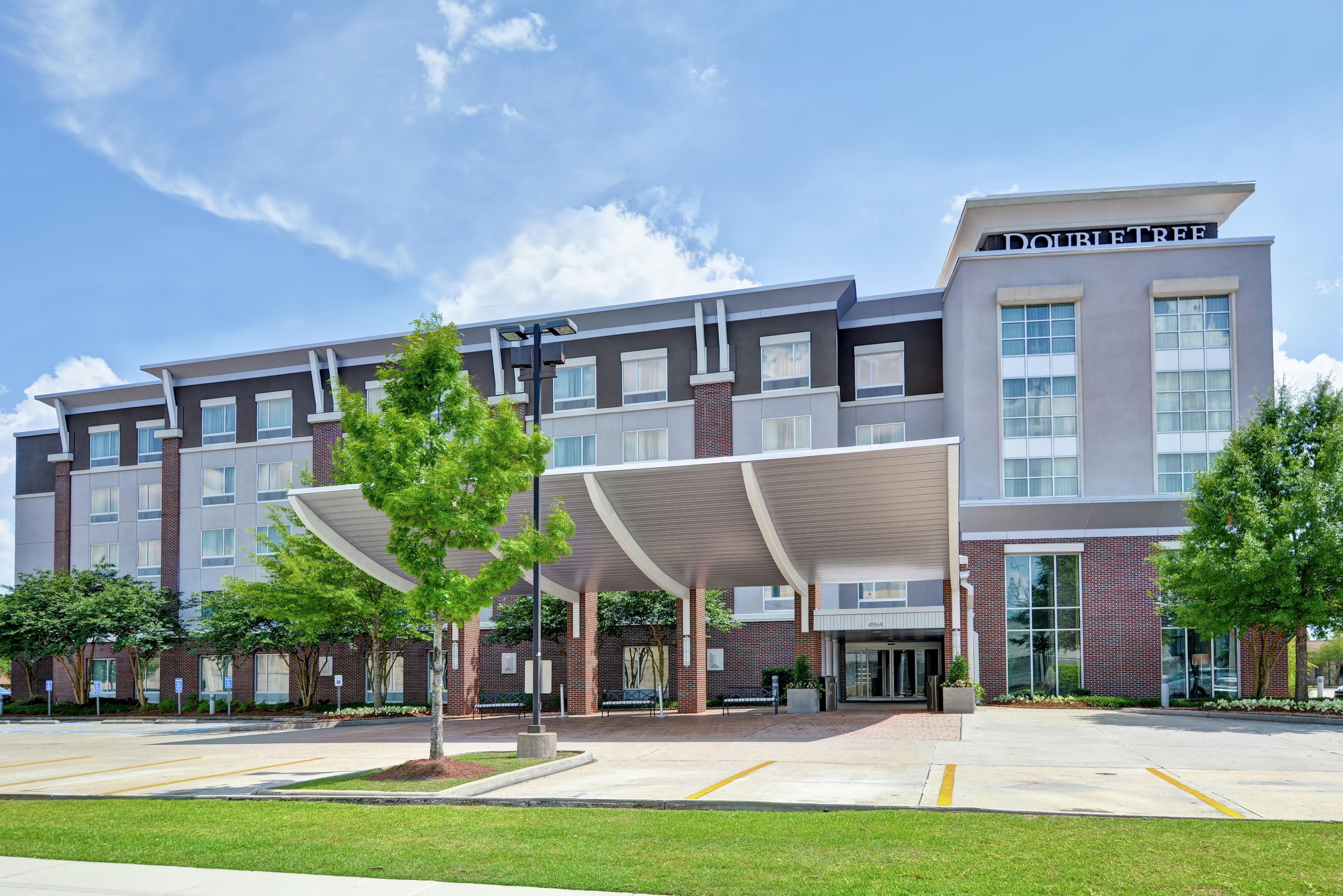 A modern hotel with a covered entrance, multiple floors, and a clear sky.