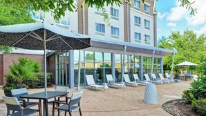A hotel patio with outdoor seating, a covered area, and a building with large windows.