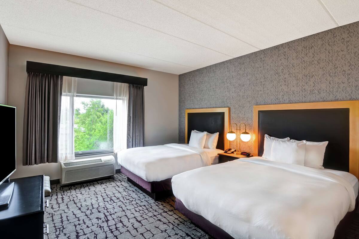 A hotel room with two beds, a TV, a heater, and a window with curtains.
