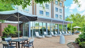 A hotel patio with outdoor seating, a covered area with patterned umbrellas, and a building with large windows. - DoubleTree by Hilton Hotel Baton Rouge (Baton Rouge)