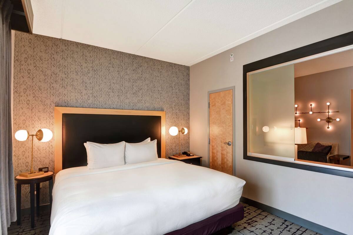 A hotel room with a large bed, two bedside tables with lamps, a mirror, and a patterned wall.