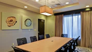 Un salón de conferencias con una larga mesa, sillas, una lámpara en el techo y dos obras de arte colgadas en las paredes.