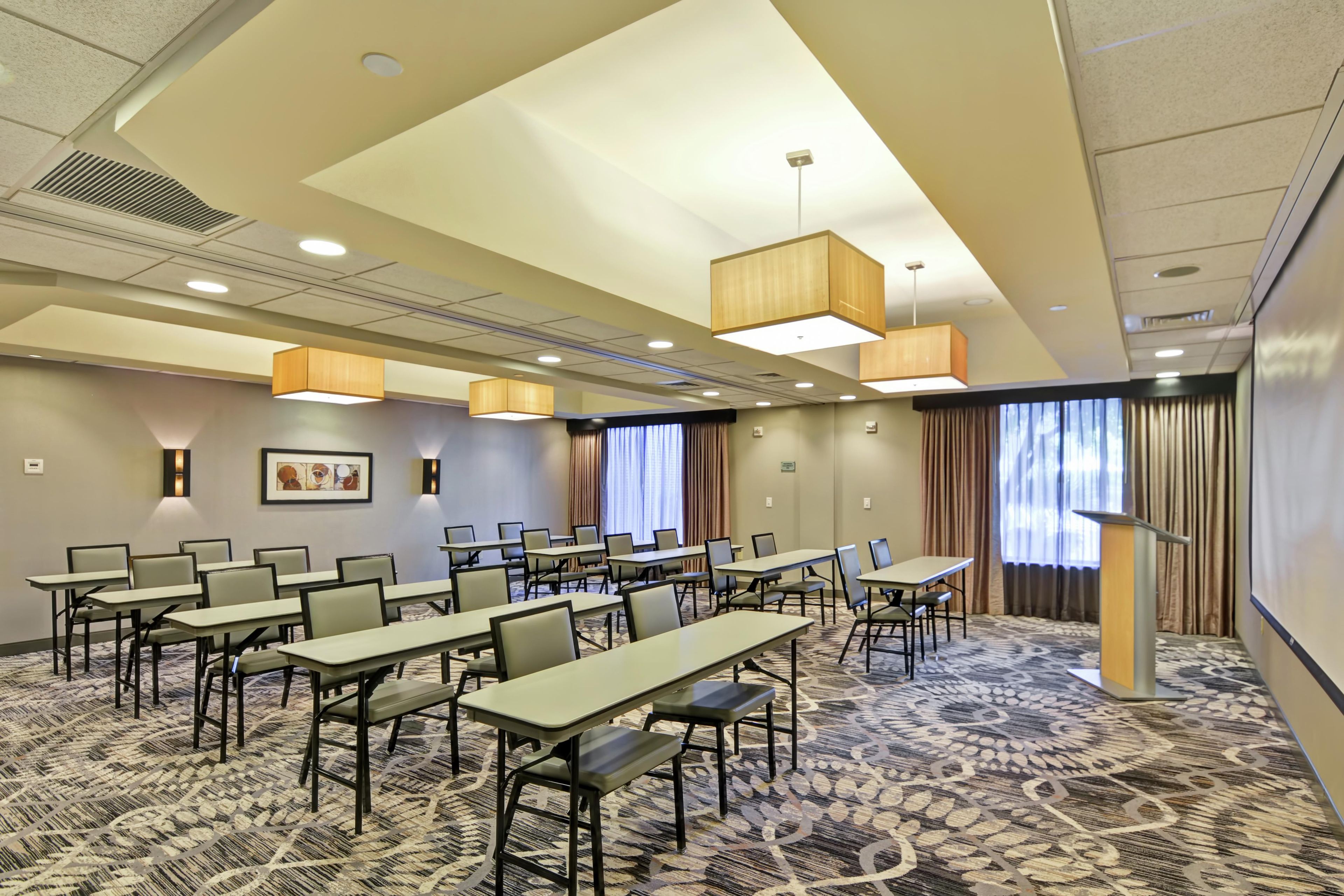 A conference room with multiple tables and chairs, a patterned carpet, and a ceiling with recessed lighting.