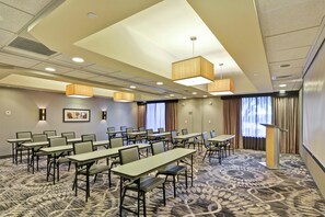 Une salle de conférence dotée de plusieurs tables et chaises, d’un tapis à motifs et d’un plafond équipé d’un système d’éclairage encastré.