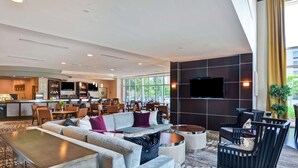 A modern hotel lobby with a seating area, a bar, and a kitchen in the background.