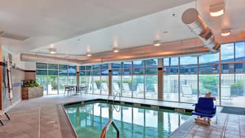 Una piscina interior con paredes de vidrio transparente, un área de descanso junto a la piscina y vistas al exterior.