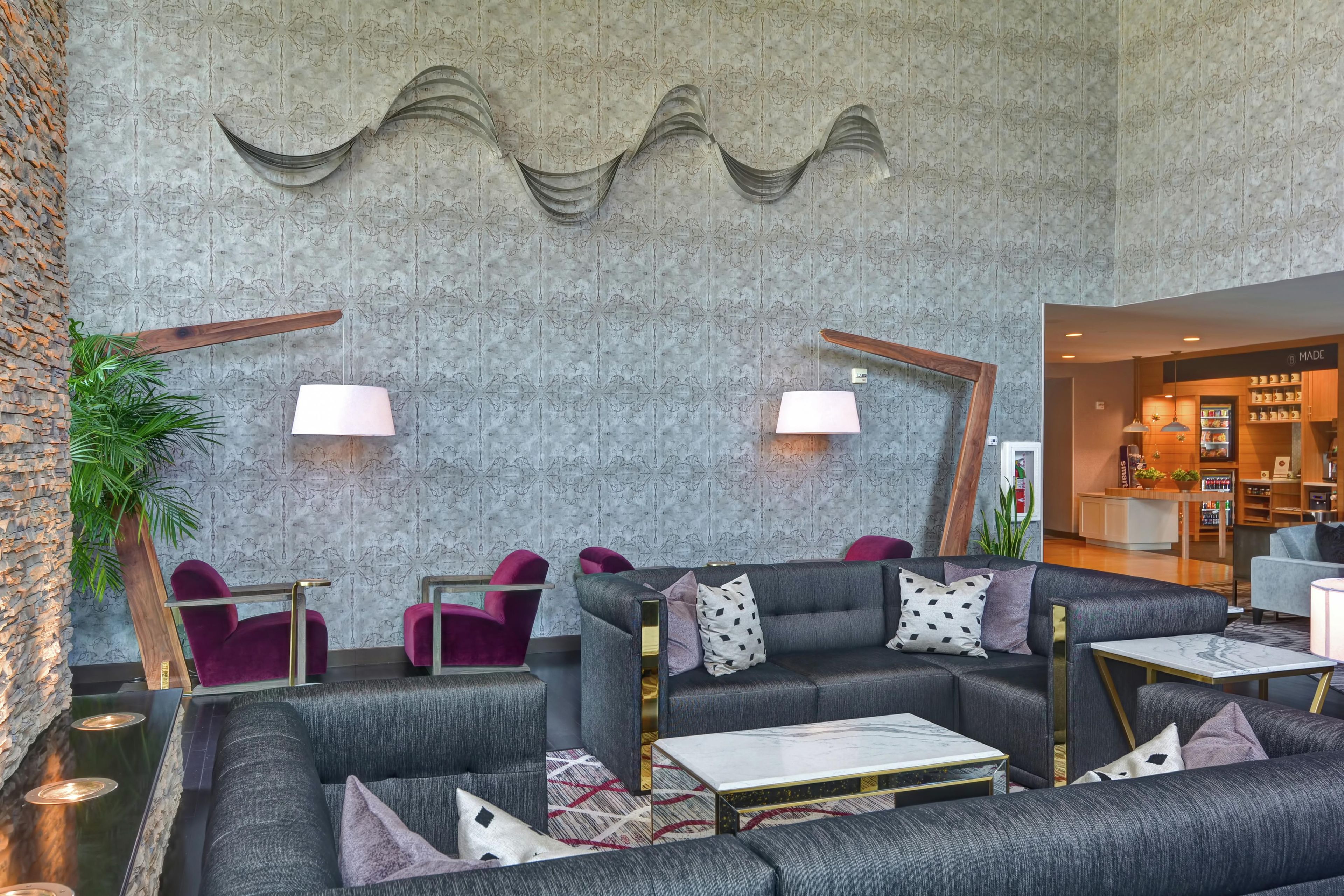 A modern lobby with a grey patterned wall, seating area with grey sofas and red chairs, and a reception desk in the background.