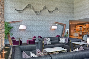 Un moderno vestíbulo con pared de diseño gris, zona de estar con sofás grises y sillones rojos, y un mostrador de recepción al fondo.
