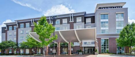 A modern hotel with a covered entrance, multiple floors, and a clear sky.