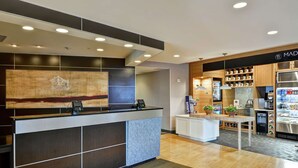 A hotel reception area with a modern design, including a reception desk, a large abstract painting, and a coffee station.