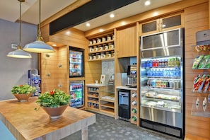 Une cuisine moderne et compacte, dotée de meubles en bois, d’un réfrigérateur en acier inoxydable et de divers distributeurs de nourriture et de boissons.
