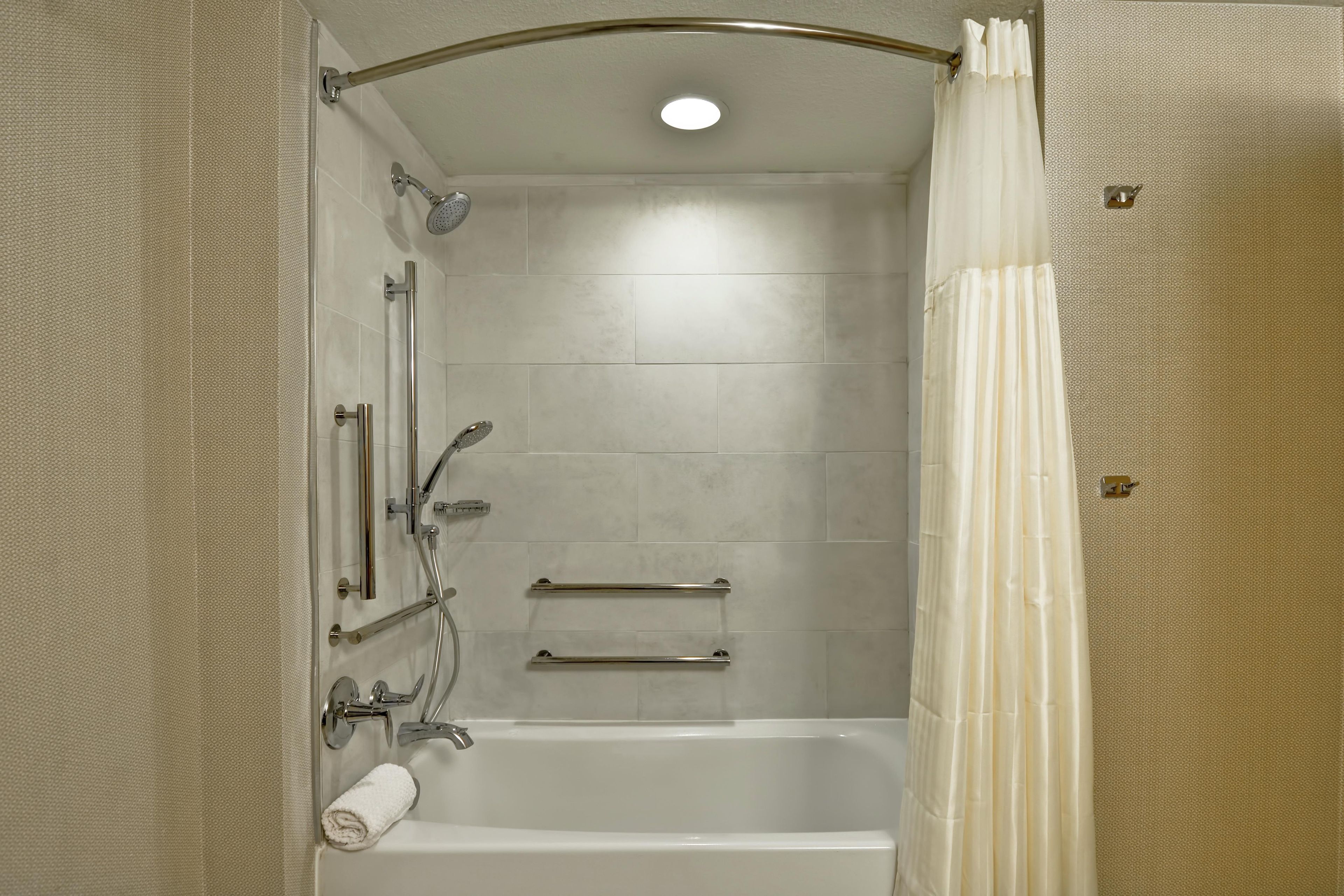 A bathroom with a bathtub, shower, and handrails.