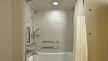 A bathroom with a bathtub, shower, and handrails.