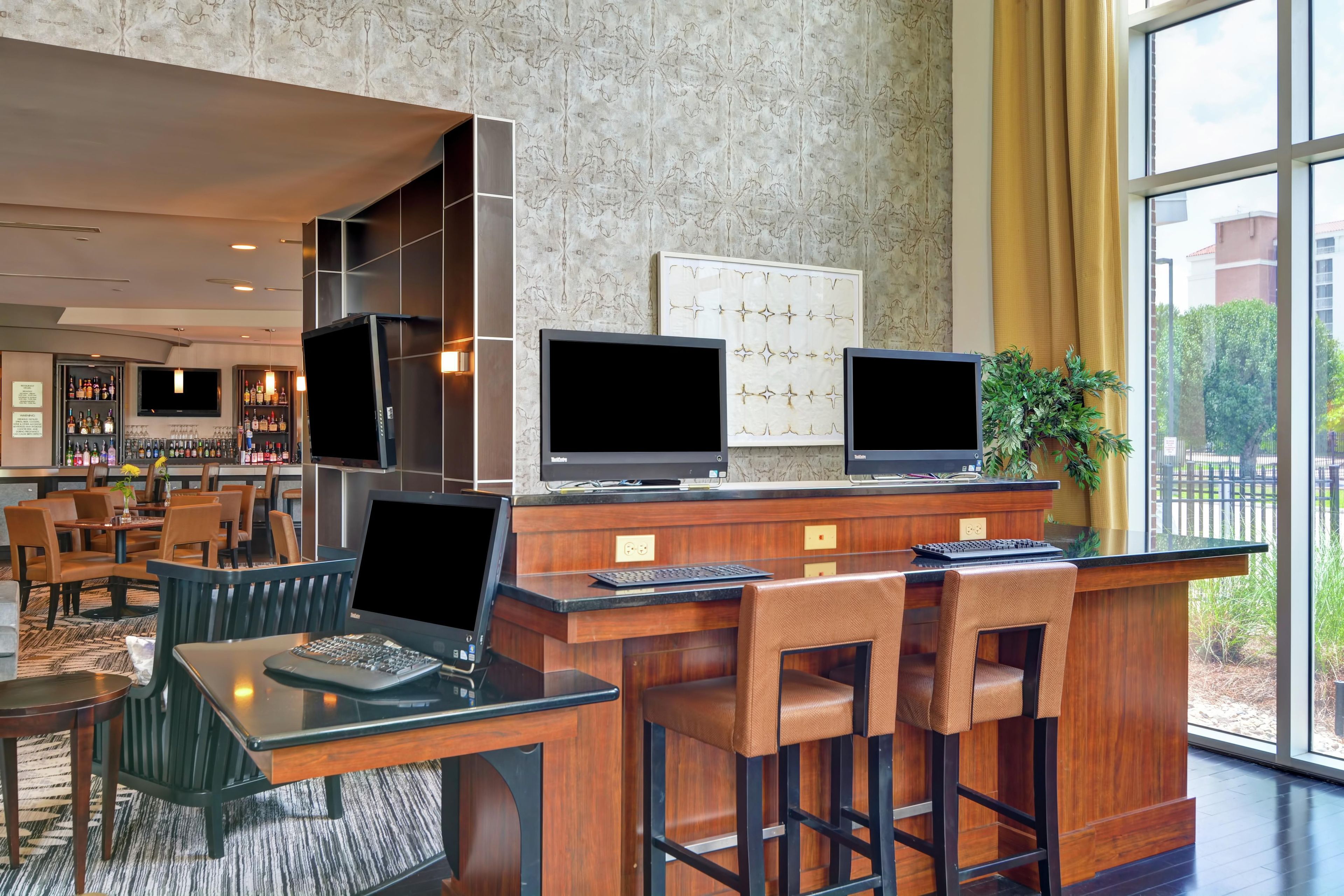 Bar e lounge de hotel com diversas opções de assento, balcão com variedade de garrafas e uma grande janela com vista para o exterior.