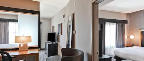 A hotel room with a bed, a desk with a lamp, a chair, a TV, and a large mirror.