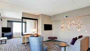 A hotel room with a bed, a desk, a chair, a sofa, a small table, a mirror, and a wall-mounted light fixture.