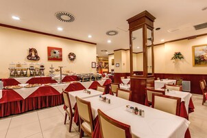 A dining area with multiple tables, some covered with red tablecloths, and a buffet setup with various food items.