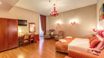 A hotel room with a wooden floor, a bed with orange bedding, a desk with a chair, a television, and a chandelier.