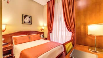 Una camera d'albergo con un letto grande, una scrivania con una lampada, una sedia e un quadro appeso al muro.