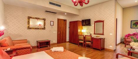 A hotel room with a large bed, a sitting area with a sofa, a desk with a chair, a TV, and a mirror.